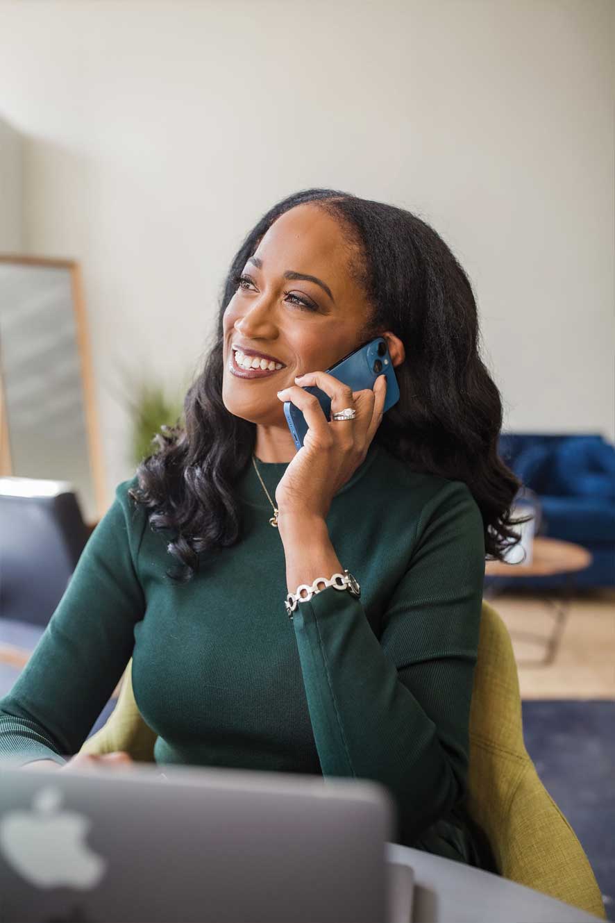 Ugochi on her phone, in a green dress with a bright smile.