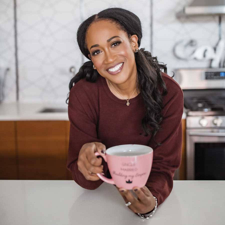 Ugochi, a dark-skinned woman in a maroon sweatshirt holding a pink mug and smiling so brightly