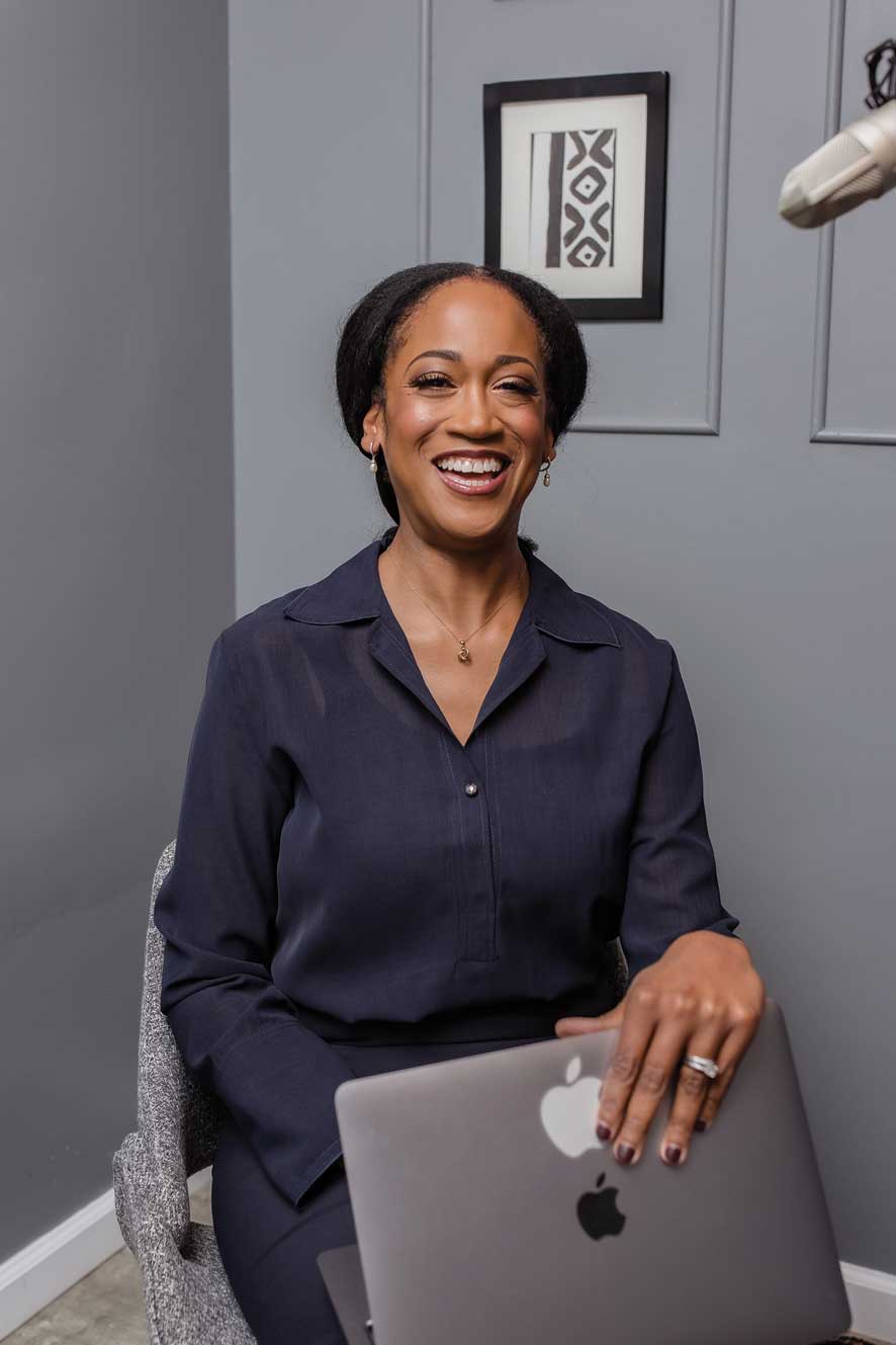 Ugochi wearing a navy blue skirt and shirt, smiling brightly with a MacBook half opened on her laps